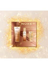 Zestaw prezentowy NUXE zawierający trzy produkty: złoty olejek do ciała, spray zapachowy oraz krem, w brązowym pudełku z złotymi akcentami i błyskotkami.