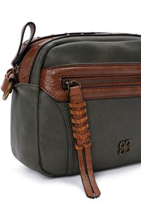 Sac en cuir vert olive avec des accents en cuir marron, anse supérieure, compartiment zippé, détail tissé sur la tirette du zip et logo discret.