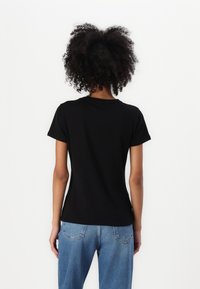 T-shirt nera a maniche corte con scollatura rotonda, realizzata in tessuto morbido. Abbinata a jeans in denim azzurro chiaro a vita alta.