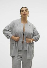 Grijze op maat gemaakte pak met een relaxte pasvorm, bestaande uit een blazer met grote revers, een cropped top met striksluiting, en wijde broekspijpen. Soepele textuur.