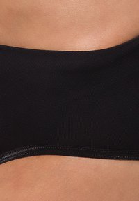 Černý bikiny top vyrobený z hladkého a elastického materiálu, s bezešvým designem a nízkým pruhem, který zvýrazňuje pleť nositelky.