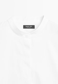 Bílé tričko s malým stojáčkem a knoflíkem, na kterém je černý štítek s nápisem "Massimo Dutti Made in Morocco."