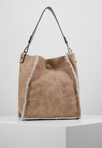 Tanfarvet bucket-taske i imiteret ruskind med hvid imiteret pels langs kanterne, rund lukning øverst og en enkelt skulderrem med metalhardwaredetaljer.