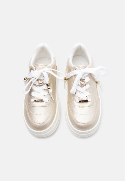 Ζευγάρι μεταλλικά χρυσά χαμηλά αθλητικά παπούτσια με λευκά κορδόνια, χρυσούς μικροαντικαταστάτες λογότυπου και χοντρές λευκές σόλες σε ανοιχτό φόντο.