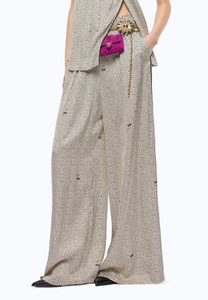 Pantalones anchos beige con pequeños puntos negros y motivos sutiles, combinados con un top a juego, cinturón dorado con detalle de rayos de sol y una pequeña bolsa morada.