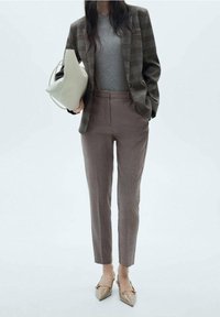 Blazer à carreaux dans des tons de marron, t-shirt gris, pantalon marron ajusté et ballerines beiges à bouts pointus. Tenant un sac à main gris clair avec une anse.