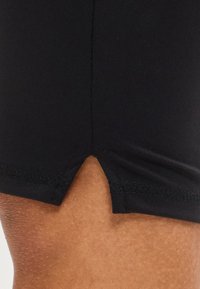 Κοντινό της άνω μηρού ενός ατόμου που δείχνει μαύρα σορτς με μικρή τριγωνική κοπή στο τελείωμα.