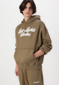Olivgrüner Kapuzenpullover mit Fronttasche, gesticktem "Low Lights Studios"-Logo in Weiß, entspannte Passform, gerippte Bündchen und Saum.