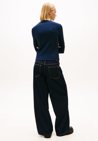 Μπλε ριμπ μακρυμάνικο τοπ με σκαλοδωτό τελείωμα, συνδυασμένο με σκουρόχρωμο φαρδύ τζιν παντελόνι με δύο πίσω τσέπες και κίτρινα ράμματα.