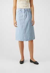 Világoskék denim midi szoknya egyenes szabással, elöl varrással és öt zsebbel. Fekete lapos cipővel és testre szabott krém színű toppal viselve.