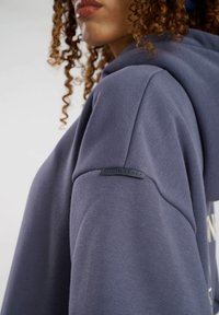 Mörkblå hoodie med en slät yta, som har en upphöjd logotyp på axeln märkt "SOUTH BEACH." Enkel design och avslappnad passform.