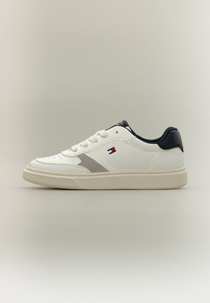 Άσπρο sneaker χαμηλού ύψους με μπεζ σόλα, μαύρο περιλαίμιο στην φτέρνα, κορδόνια και ένα μικρό κόκκινο, λευκό και μπλε λογότυπο Tommy Hilfiger στο πλάι.