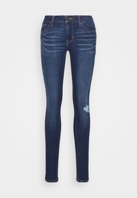 Jeans skinny blu scuro con vita media, caratterizzati da dettagli vissuti sul ginocchio sinistro e cuciture decorative ovunque.