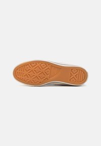 Semelle de sneaker en caoutchouc avec un design texturé en forme de diamant. Couleur orange avec des parois latérales blanches et un détail de logo subtil.