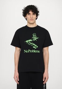 Sort bomulds T-shirt med et strålende grønt alienmotiv og teksten "No Problemo" med græsdetalje, rund halsudskæring og korte ærmer.