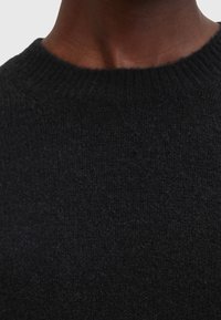 Gros plan du cou et du haut de la poitrine portant un pull noir en côtes à col rond avec un tissu tricoté texturé.