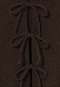 Braunes gestricktes Kleidungsstück mit einer Frontöffnung, das fünf in Schleifen gebundene Schlaufen aufweist. Weiche Textur und gerippter Abschluss an den Kanten.