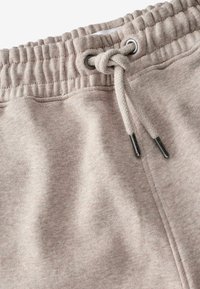 Pantalones deportivos de color beige claro con una cinturilla elástica y cordones, y ojales de metal. Tejido suave y texturizado con un acabado liso.