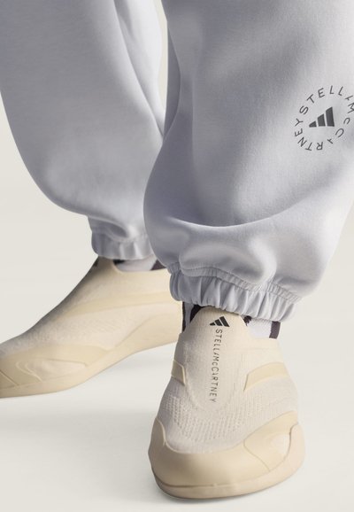 Κρεμ χρώματος sneakers slip-on με "Stella McCartney" και λογότυπο Adidas, συνδυασμένα με ανοιχτογκρι joggers με στρογγυλό λογότυπο Stella McCartney.