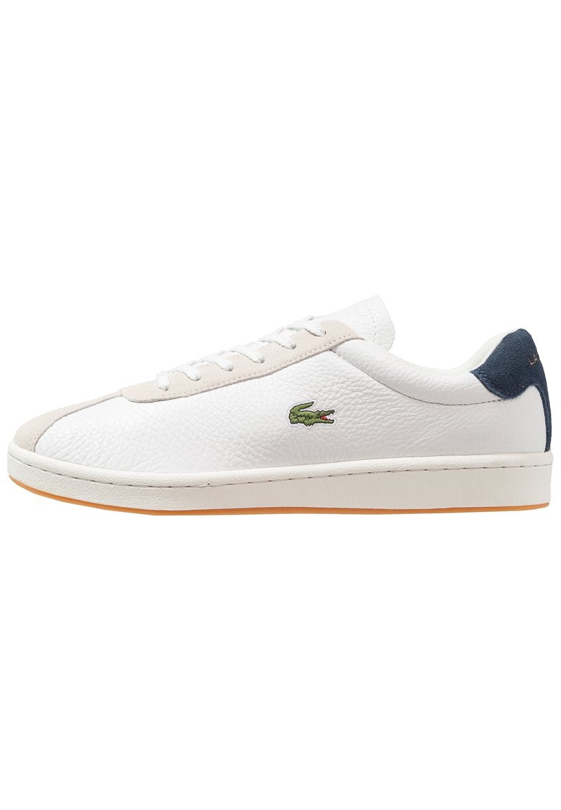 Sneakers en cuir blanc avec un fini texturé, des accents beiges, un logo crocodile vert, une languette de talon bleue et une semelle en caoutchouc orange.