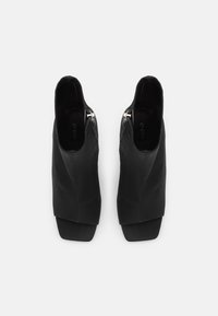 Mustat nahka nilkkurit, joissa on avoin etu, neliömäinen varvas ja hopeinen vetoketju. Silkkinen pinta ja istuva muotoilu litteällä korolla.