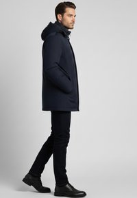 Parka impermeable azul marino con capucha, bolsillos laterales y corte recto. Combina con jeans oscuros y zapatos de cuero negros.