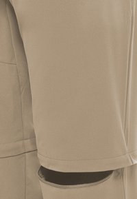 Shorts beiges à texture lisse, avec une poche arrière et des coutures surpiquées. Le design comprend un ourlet discret et une coupe ajustée.