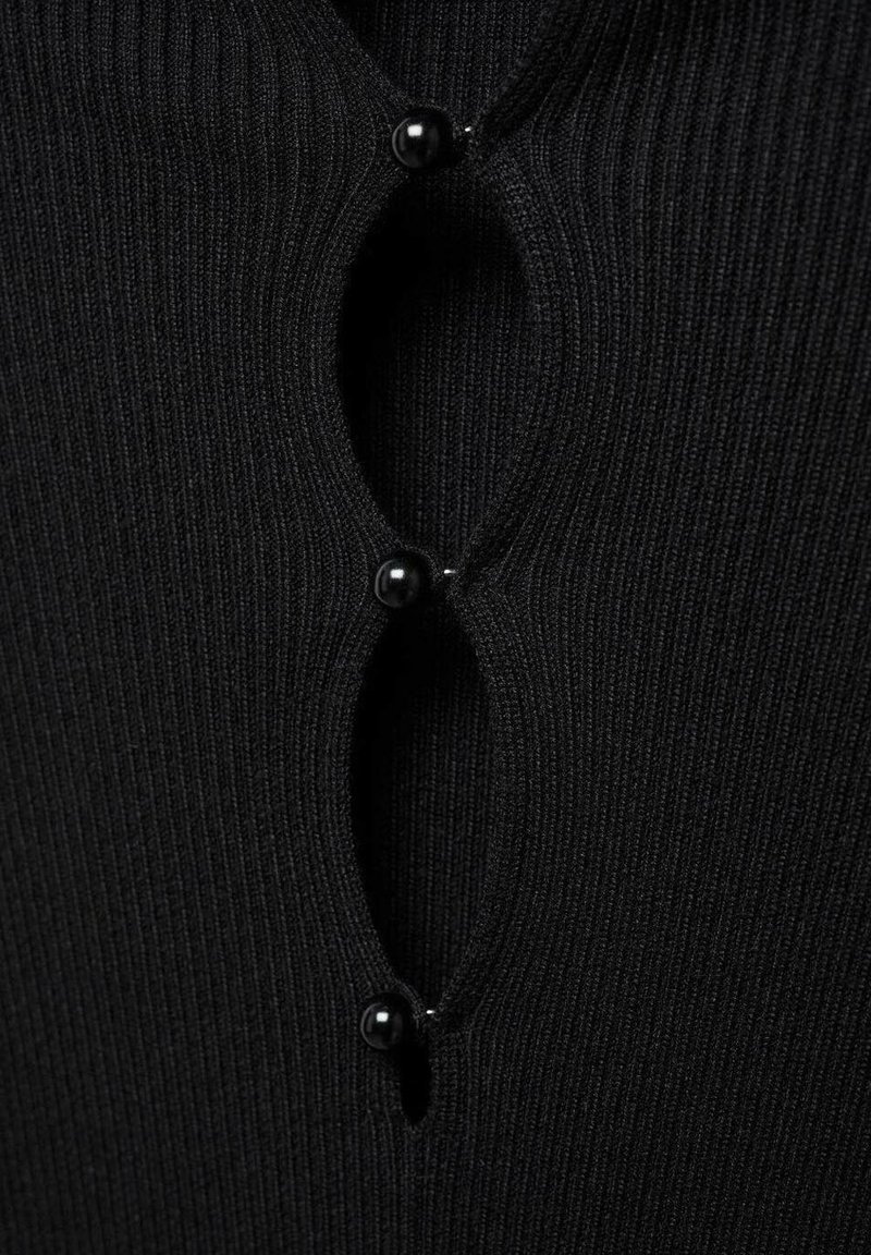 Top nero a coste con un design a chiave e due bottoni neri lucidi. La texture è fine, creando un aspetto aderente.