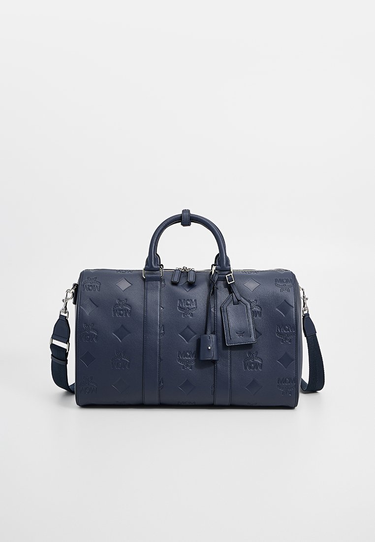 Navyblaue Leder-Reisetasche mit geprägtem Logo-Muster, zwei runden Griffen, verstellbarem Tragegurt und einem Gepäckanhänger.