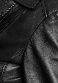 Crna kožna jakna s glatkom teksturom, strukturiranim ovratnikom i vidljivim detaljima šivanja duž šavova. Istaknuto zatvaranje na patentni zatvarač.