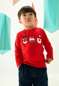 Chemise à manches longues rouge avec des motifs brodés d'un renne, de pudding de Noël et de Santa. Tissu doux, coupe décontractée.