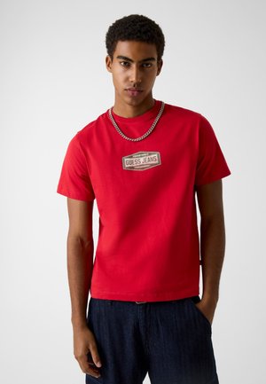 Rood katoenen T-shirt met een centrale "Guess Jeans" logo patch. Ontworpen met een ronde hals, korte mouwen en een losse pasvorm.