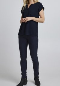 Námořnická modrá blůza s výstřihem do V a krátkými rukávy, se dvěma předními kapsami, doplněná o tmavé skinny džíny a černé kotníkové boty.