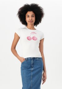 Hvit tettsittende t-skjorte med korte ermer, med ett rosa kirsebærmotiv og "Guess" tekst. Kombinert med et denimskjørt, som viser en uformell stil.