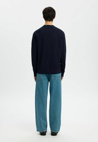 Granatowy sweter z długimi rękawami i okrągłym dekoltem; w zestawie z szerokimi niebieskimi dżinsami typu relaxed fit, które mają dwie tylne kieszenie.