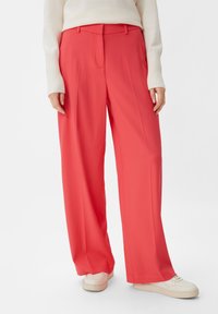 Bright coral wide-leg trousers made from smooth fabric, featuring a high waist and sharp pleats, paired with white sneakers.