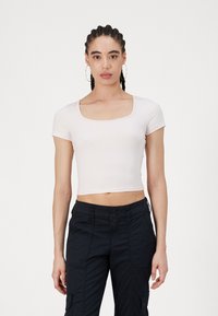 Rövid ujjú, cropped top, puha, világos rózsaszín anyagból, négyzet alakú nyakkivágással és sima felülettel, sötét cargo nadrággal párosítva.
