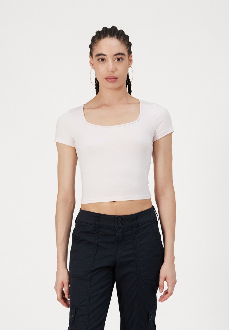 Rövid ujjú, cropped top, puha, világos rózsaszín anyagból, négyzet alakú nyakkivágással és sima felülettel, sötét cargo nadrággal párosítva.