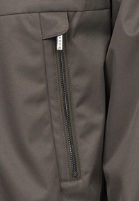 Dunkelgrauer Stoff mit glatter Textur, ausgestattet mit einer Reißverschlusstasche mit silberner Hardware. Der Reißverschluss verläuft entlang der Kante der Tasche.