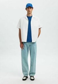 Hvid kortærmet skjorte med ternet mønster, blå t-shirt med rund hals, lyseblå løse jeans, sko i sort og hvidt, blå kasket.