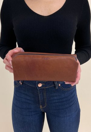 Bruin leren etui met een gladde textuur, voorzien van een ritsluiting en subtiele branding aan de voorkant. Rechthoekige vorm, middelgroot formaat.