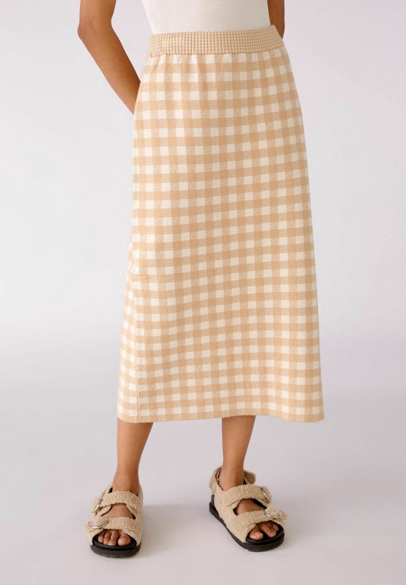 Falda midi a cuadros en beige y blanco con una cintura fruncida y bolsillos laterales, combinada con sandalias de peluche beige. Tejido texturizado.