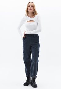 Witte blouse met lange mouwen en een uitsnijding aan de voorkant, gecombineerd met navy cargobroek met zijzakken en een verstelbare onderrand. Zwarte combat boots.