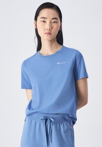 T-shirt di cotone azzurro chiaro con maniche corte, collo a giro e un piccolo logo sul petto. Tessuto liscio e vestibilità rilassata.