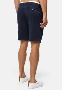 Marineblå bomulds-shorts med lige snit, der har to baglommer og en glat tekstur. Sammen med hvide slip-on sko.