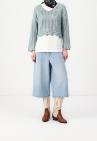 Neulottu mintunvihreä lyhyt neule, valkoinen t-paita alla, vaaleansiniset leveälahkeiset farkku shortsit, ruskeat nilkkurit ja kuvioidut kerma-väriset sukat.