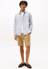 Lichtblauwe button-up shirt, witte t-shirt eronder, khaki shorts, donkere loafers. Glad stof, casual pasvorm, met een klein logo op het shirt.