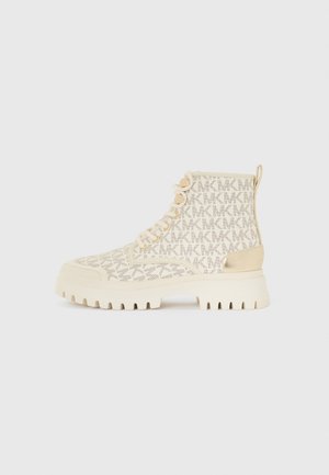 Botas de tobillo beige con un patrón texturizado, con una suela gruesa, acentos dorados y cordones tradicionales. Tacón trasero elevado para mayor soporte.
