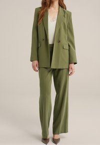 Olivově zelený saka se zapínáním na dvojité knoflíky a předními kapsami, spojené s odpovídajícími širokými kalhotami a krémovým topem s krajkovým lemem.