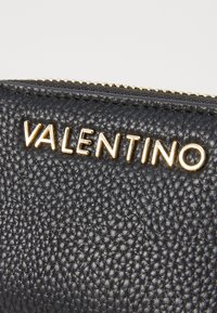 Must mustriga nahast rahakott, millel on kuldne "VALENTINO" kiri, ülemine lukuga sulgemine ja kareda pinna detail.